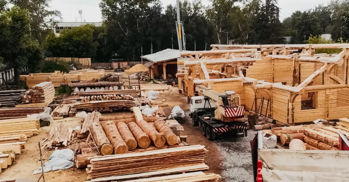 A timber construction yard with stacked logs, sawn boards and a crane